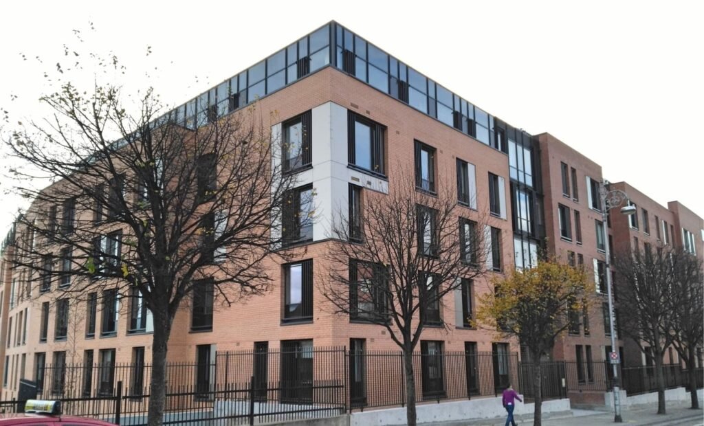 Modern brick apartment building with glass top floor and street trees.