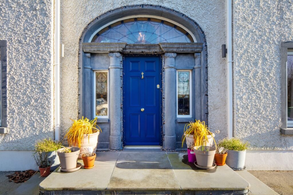 Blue front door with arched fanlight and potted plants.