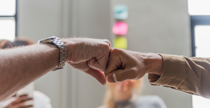 Close-up of two colleagues giving a fist bump in a modern office environment.
