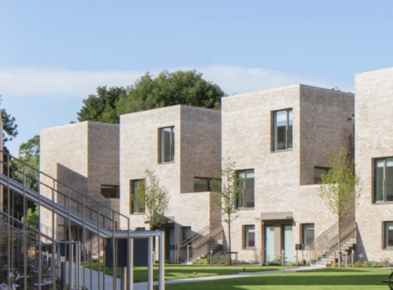 Row of contemporary beige brick townhouses with metal outdoor staircases and young trees set along a green lawn.