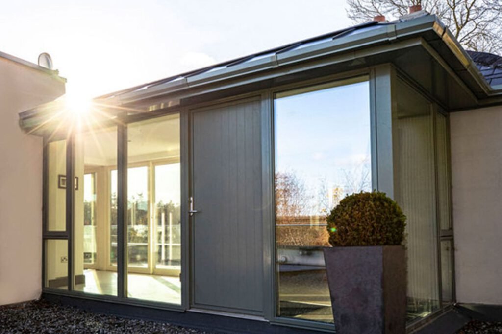 Modern home extension with large glass windows and a grey door illuminated by bright sunlight.