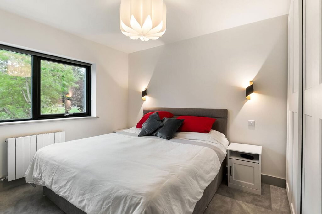 Modern bedroom with a double bed, red and grey pillows, wall sconces, and a flower-shaped ceiling light.