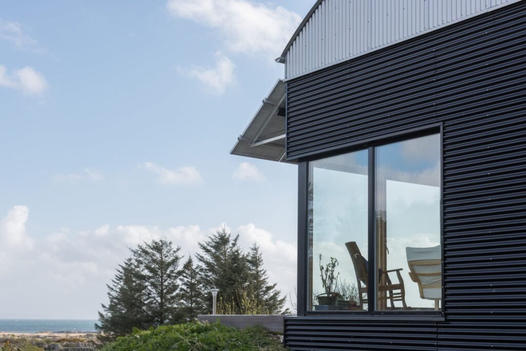 Modern home with black corrugated metal cladding, a curved barrel roof, large glass windows, and roof-mounted solar panels.