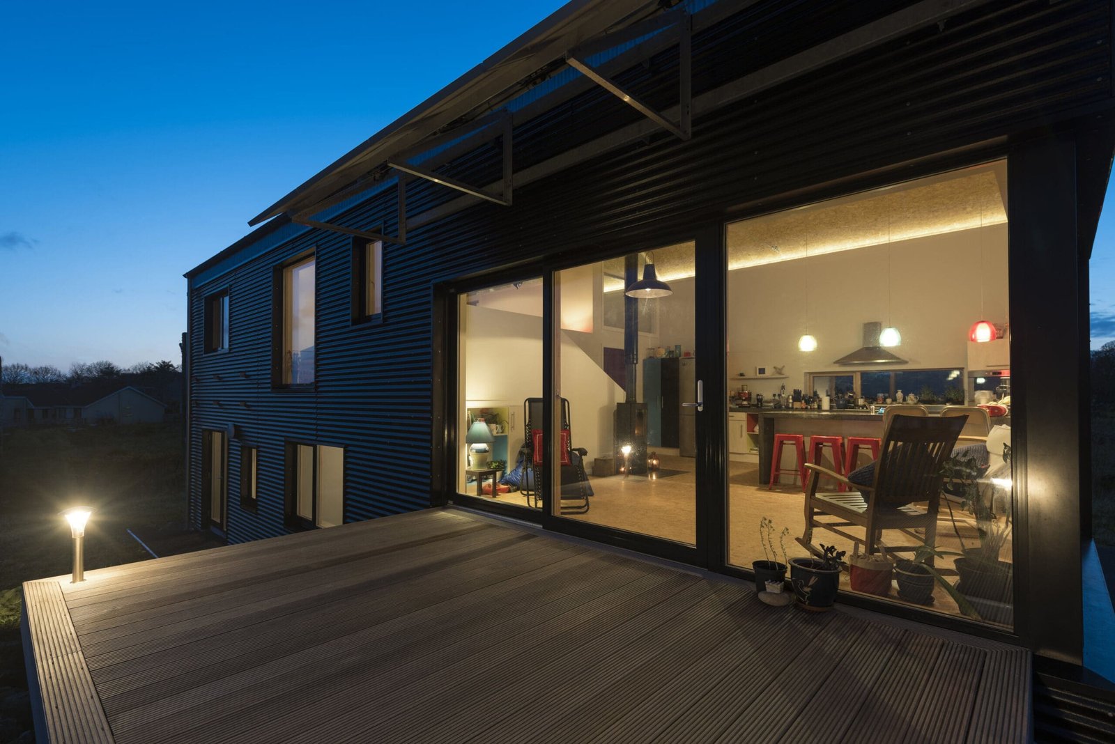 Modern home with black corrugated metal cladding, a curved barrel roof, large glass windows, and roof-mounted solar panels.
