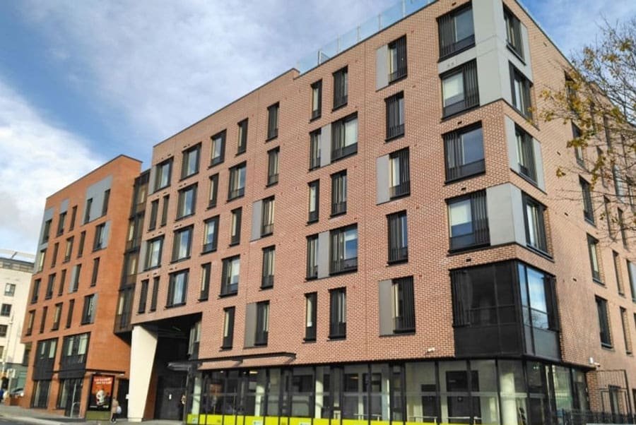 Modern brick apartment building with glass top floor and street trees.