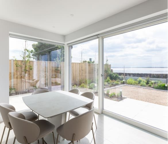 Bright modern dining room with large windows overlooking a coastal garden and sea view.