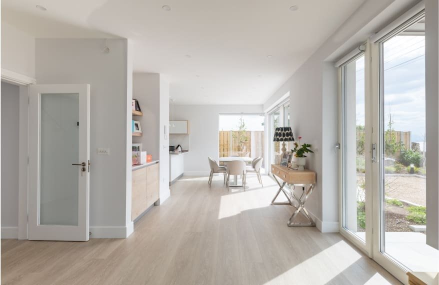 Open-plan modern home interior with light wood flooring, dining area, and large glass patio doors.