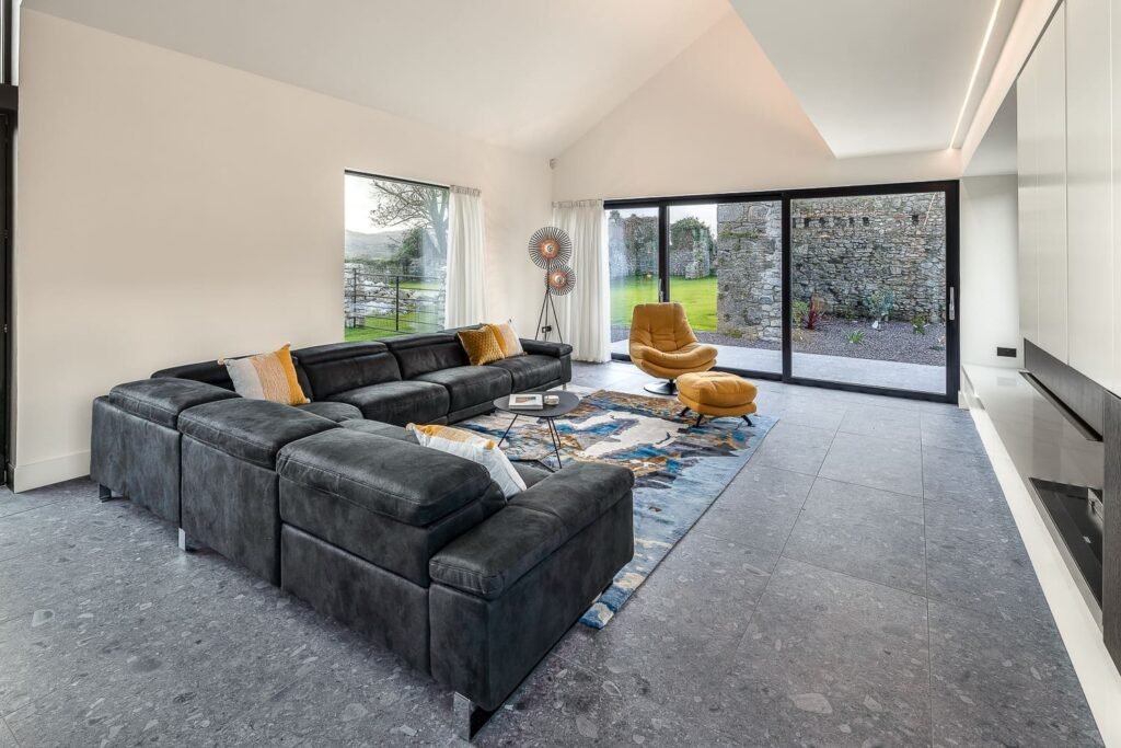 A living room with a black couch, golden chair golden pillows and a dark grey flooring.