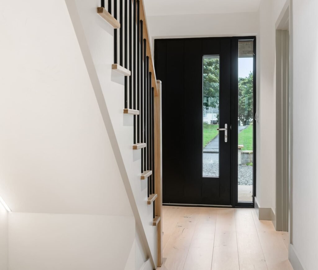 A hallway with white and wood stairs and a black door.