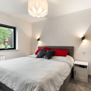 Modern bedroom with a black-framed window overlooking trees, a radiator, and a bed with a red cushion.
