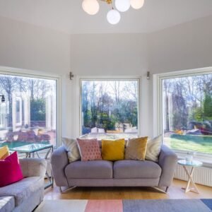 Bright sitting room with grey sofas, colourful cushions, and bay windows.