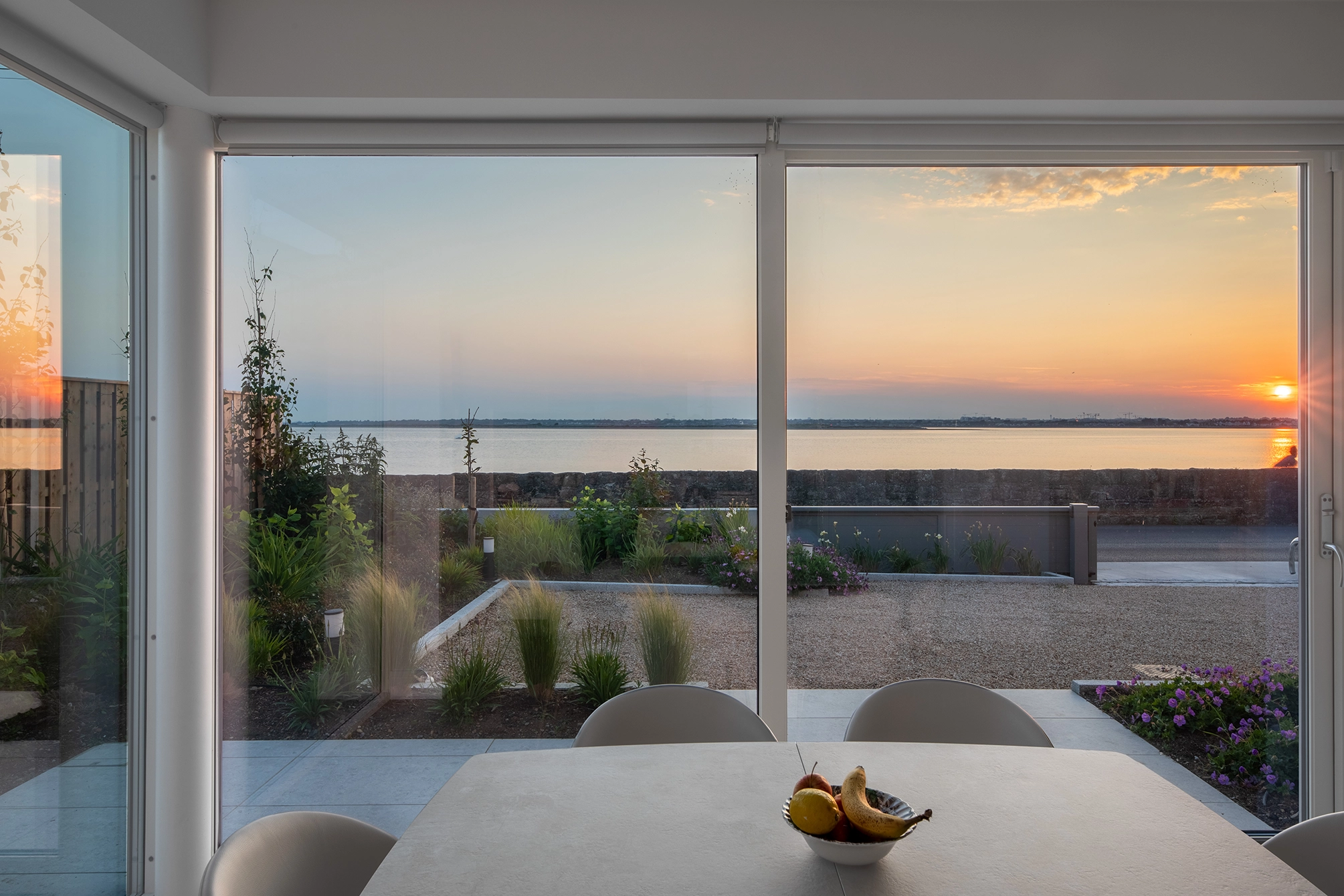 Sunset view over the sea through large glass doors from a modern dining room.
