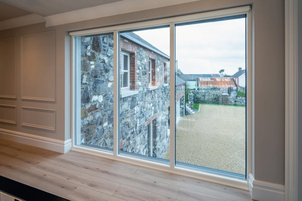 Large floor-to-ceiling picture window overlooking a stone building courtyard and gravel driveway.